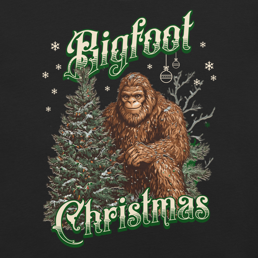 Bigfoot Christmas t-shirt featuring a friendly Bigfoot standing beside a decorated evergreen tree with snowflakes falling, text reads “Bigfoot Christmas” in green and white vintage lettering on a black tee.