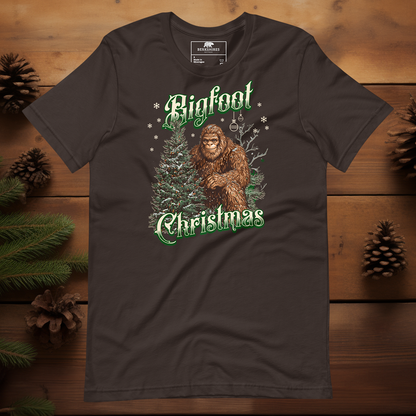 Funny Bigfoot Christmas t-shirt in brown showing a festive forest scene with Bigfoot and a Christmas tree, vintage green lettering and snowflakes for a cozy woodland holiday feel.